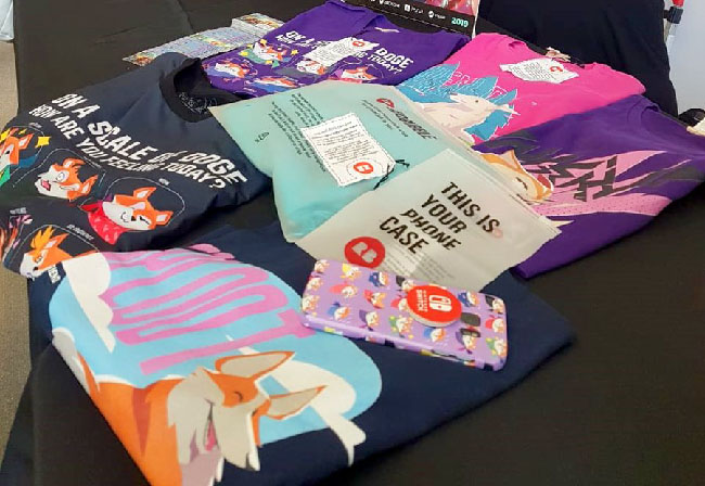 Colorful clothes illustrated with dogs laid out on a booth table. There is also a purple phone case with a dog pattern on it.