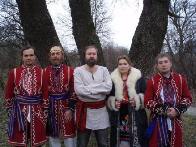 A photo of Rodnovery, a celebration of the pre-Christian traditions of Slavic Europe. It features five people; three of them are mostly dressed in red, one is in white, and the last is in a dark coat with a fluffy white collar.